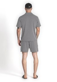 Conjunto de camiseta de manga corta y pantalones cortos en blanco y negro con un patrón geométrico, fabricado en tejido ligero, diseñado para uso casual.