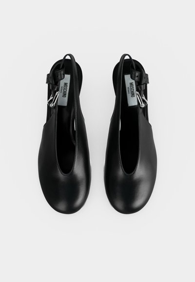Ζευγάρι μαύρα δερμάτινα slingback παπούτσια Moschino με στρογγυλεμένες μύτες και ασημένιες αγκράφες σε λευκό φόντο.