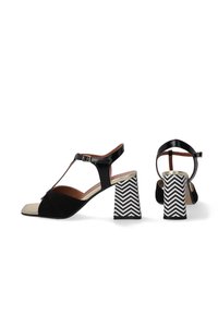 Schwarze Wildledersandalen mit einer glänzenden goldenen Zehenpartie, T-Riemen-Design und einem gemusterten weiß-schwarzen Zickzack-Blockabsatz. Verstellbarer Knöchelriemen.