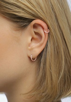Rosaguld metal hoops hængende fra øret, der har en glat overflade og et simpelt, afrundet design.