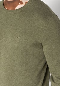 Maglione lavorato a maglia verde oliva con colletto rotondo, texture a coste e piccolo logo sul petto. Tessuto morbido con vestibilità casual.