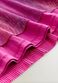 Ráncos anyag élénk rózsaszínben, kontrasztos sima részekkel. Fényes szálak futnak a redőkön, textúrát és vizuális érdekességet teremtve.