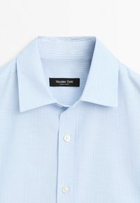 Chemise bleu clair à fines rayures verticales blanches et boutons blancs, avec un col spread et une étiquette intérieure noire.