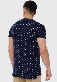 Camiseta azul marino con patrones de diamantes blancos, de manga corta y con dobladillo redondeado. Fabricada con un tejido suave para mayor comodidad y libertad de movimiento.