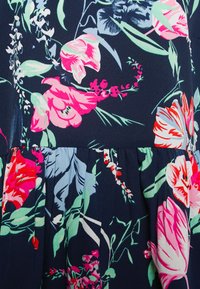 Vestido floral com flores vibrantes em rosa e azul sobre um fundo azul-marinho. Tecido leve e texturizado com pregas na barra.