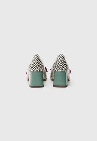 Patterned high-heeled shoes featuring a geometric black and white design, a teal block heel, and pink decorative accents.