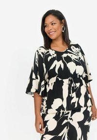 Haut à motif floral noir et blanc avec des manches courtes, une taille nouée et une coupe décontractée. Fabriqué en tissu léger avec une texture lisse.
