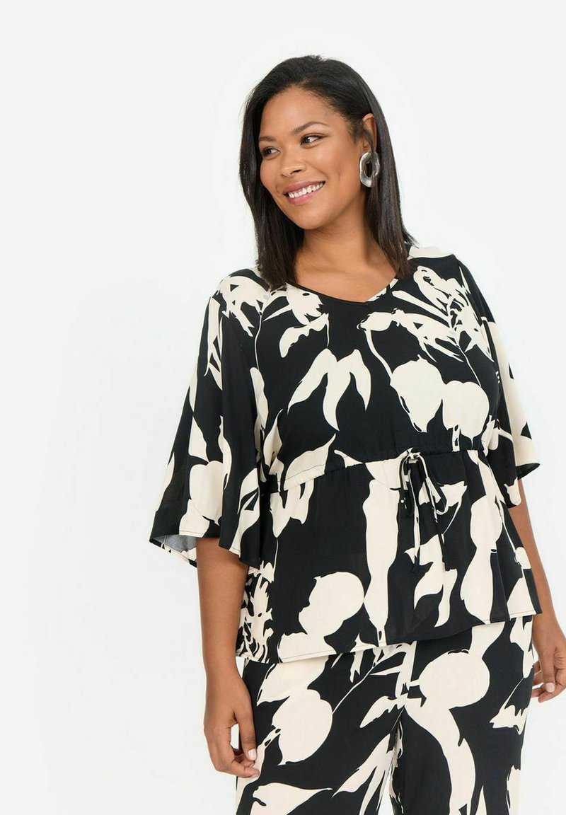 Haut à motif floral noir et blanc avec des manches courtes, une taille nouée et une coupe décontractée. Fabriqué en tissu léger avec une texture lisse.
