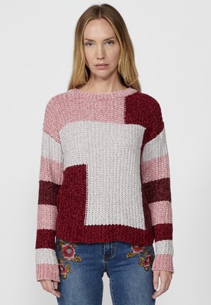 Pull en tricot avec un design en blok de couleur comprenant des nuances de rose, rouge et gris. Coupe ample, col rond et poignets côtelés.