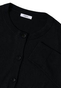 Zwarte cardigan met rond decolleté, voorzien van vijf knopen en een zak. Gemaakt van zacht materiaal met een geribbeld kraag en mouwen. Etiket zegt "CECIL."