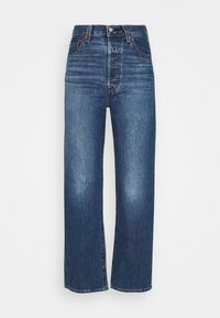 Jean bleu taille haute à jambes droites avec poches avant, fermeture par boutons et légère décoloration sur les cuisses sur fond blanc.