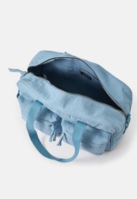 Blaue Kordtasche mit einem Reißverschluss, zwei robusten Griffen und einem geräumigen Innenraum. Sie verfügt über eine wellige Textur und kleine hängende Quasten.