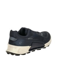 Navy blue athletic shoe with a textured upper and Gore-Tex branding. Features a cushioned, light beige sole and black traction outsole.