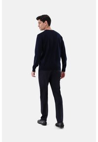 Marineblauer Pullover mit Rundhalsausschnitt, gerippten Bündchen und Saum, kombiniert mit eng anliegenden dunklen Hosen und schwarzen Schuhen, von hinten betrachtet.