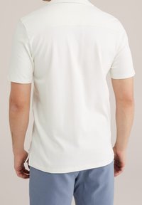 Vit pikétröja med korta ärmar i ett mjukt, strukturerat tyg, med sidöppningar i fållen och en diskret detaljering vid axeln bak.