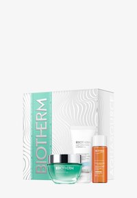 Zestaw kosmetyków Biotherm w białym pudełku z falistym wzorem. Zawiera zielony żel, białą krem oraz pomarańczowy olejek, ukazując różnorodne tekstury.