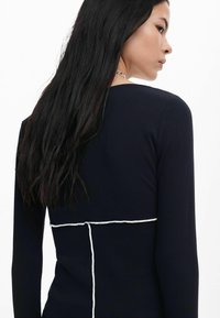 Mornarski dukserica s dugim rukavima i rebrastom teksturom. Ima kontrastne bijele šavove duž struka i leđa, ističući siluetu.