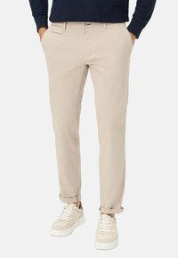 Beige chinos met een slim fit, voorzien van een ritzak, ceintuurlussen en opgerolde manchetten, gecombineerd met schoenen in neutrale tinten.