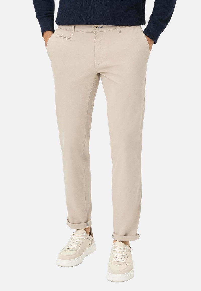 Beige chinos met een slim fit, voorzien van een ritzak, ceintuurlussen en opgerolde manchetten, gecombineerd met schoenen in neutrale tinten.