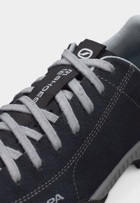 Κοντινό πλάνο ενός σκούρου γκρι αθλητικού παπουτσιού με ανοιχτό γκρι κορδόνια, λευκό ραφές και μαύρη ετικέτα με την επωνυμία "RESHOES" στη γλώσσα.