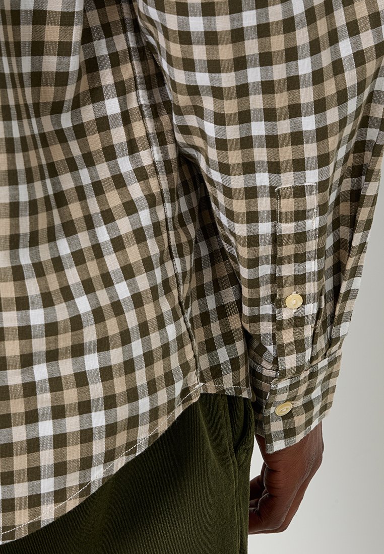 Bruin en beige geruit overhemd met een knoopmanchet en een gebogen zoom, gemaakt van lichtgewicht stof, gelaagd over donkergroene broeken.