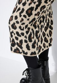 Jupe tricot beige et noire à imprimé léopard, portée avec des leggings noirs et des bottines noires lacées avec fermetures éclairs.