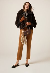 Brązowa kurtka z sztucznego futra, kwiatowa bluzka, brązowe spodnie z wysokim stanem, brązowe rękawiczki, czarne baleriny z łańcuszkiem oraz mała brązowa torebka z szalikiem.