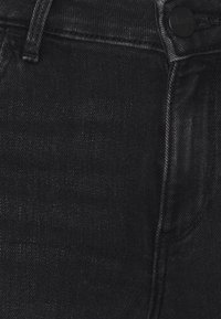 Pantalones vaqueros de mezclilla negra con una textura suave, diseño clásico de cinco bolsillos y cierre de botón en la cintura.