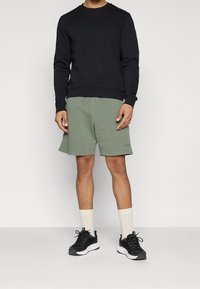 Sweat-shirt noir à col ras du cou, short vert olive, baskets noires et chaussettes beige. Style sportif décontracté, en coton.