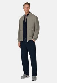 Giacca bomber grigio chiaro con colletto alto, zip frontale e due grandi tasche. Abbinata a pantaloni blu navy e scarpe sportive grigie.