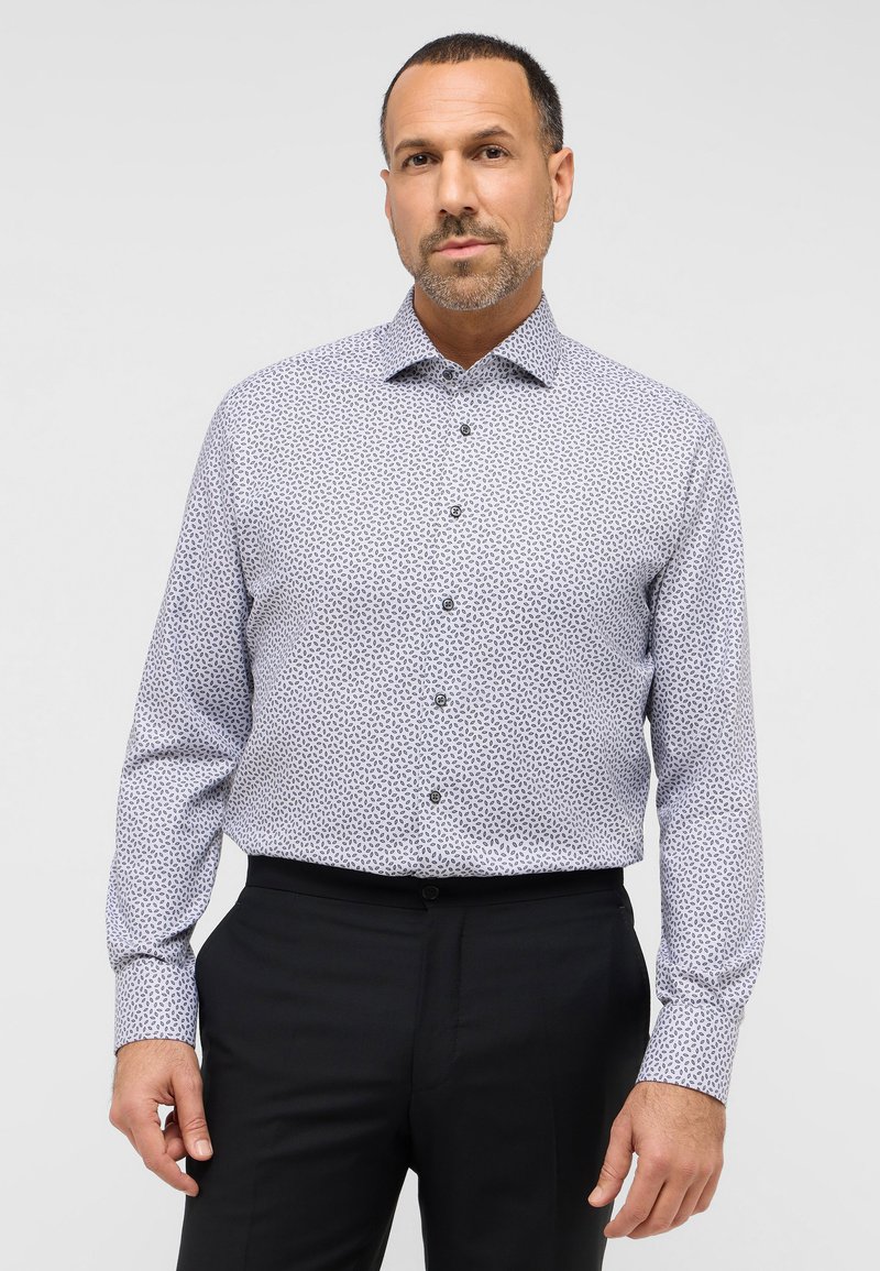 Weißes Hemd mit einem marineblauen Blattmuster, langen Ärmeln und einem Button-Down-Kragen, kombiniert mit schwarzen Hosen. Textilstruktur mit glatter Oberfläche.