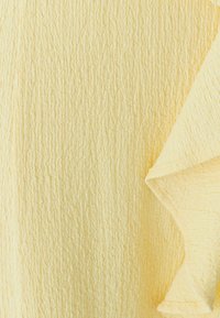 Textured fabric in pale yellow, featuring a crinkled pattern with a ruffled edge. Soft material with a subtle sheen and varied surface texture.