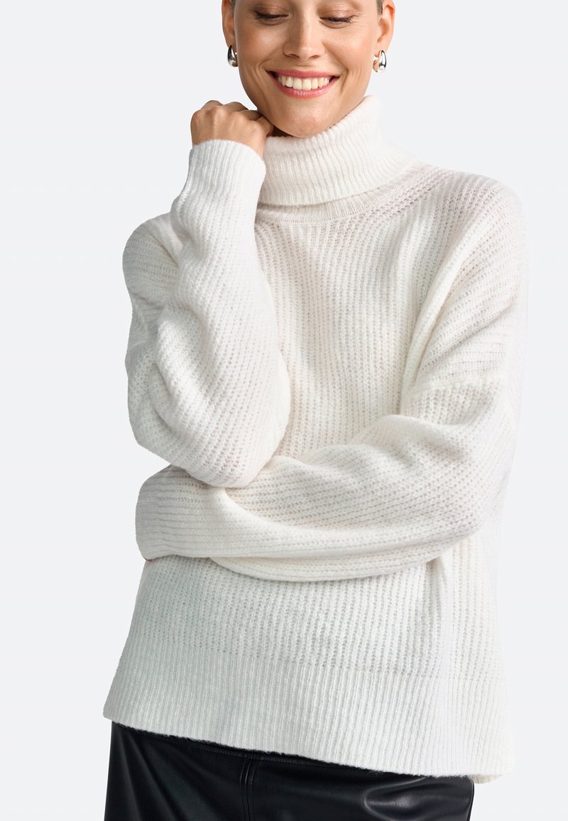 White ribbed turtleneck sweater with a relaxed fit, featuring a textured pattern and rolled cuff detail, paired with a black leather skirt.