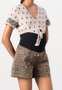 Top corto de color beige claro con cierre de botones y patrones negros, combinado con pantalones cortos de estampado de leopardo que tienen bolsillos frontales y un botón de metal.