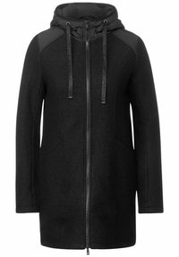 Abrigo negro con capucha, con cierre de cremallera, bolsillos laterales y detalles en los hombros a contraste. Confeccionado en tela texturada con un forro suave.