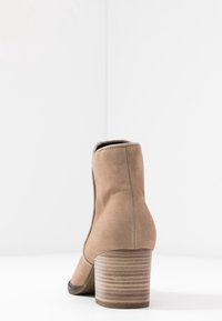 Brązowy zamszowy botek za kostkę z okrągłym noskiem, elastycznymi panelami bocznymi oraz teksturowanym, paskowanym obcasem. Gładkie wykończenie wnętrza.