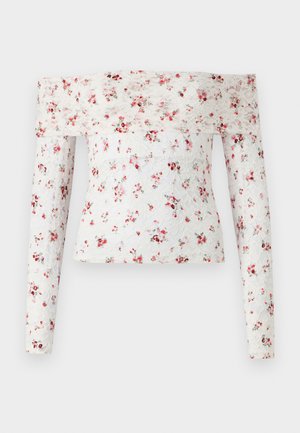 Off-shoulder blommig topp i spets, prydd med röda och gröna blommönster på vit bakgrund, med lång ärm och en figurnära design.