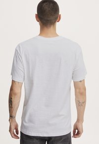 Camiseta de algodón blanca con un ajuste relajado, mangas cortas y cuello redondo. Textura suave, mínima marca y detalles de costura claros.