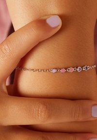 Silver chain bracelet featuring alternating pink and purple heart-shaped beads, set against a skin tone background with a light texture.