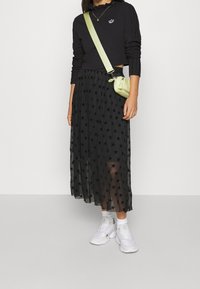 Svart plisserad kjol med stjärnmönster, kombinerad med en figurnära svart tröja och vita sneakers. Accessoarerna inkluderar en liten grön väska och ett halsband.