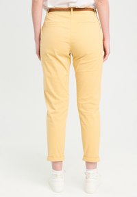 Pantalon en coton jaune au design ajusté, avec des poignets retroussés et deux poches arrière. Associé à des baskets blanches et des chaussettes à motifs.