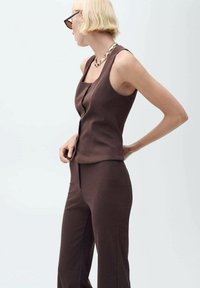 Top sans manches marron avec une coupe droite et des boutons sur le devant, associé à un pantalon taille haute assorti, en tissu doux.