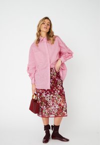 Pink striped button-up shirt with voluminous sleeves, paired with a burgundy floral printed sheer skirt, brown socks, and maroon shoes.