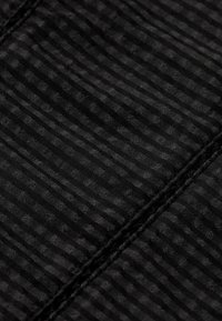 Zwarte stof met een gestructureerd ontwerp met horizontale strepen en kleine, verhoogde stippen. Gestikte naad zichtbaar langs de rand.