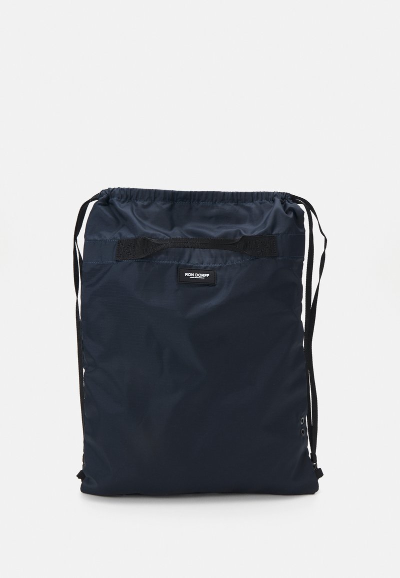 Sac à dos à cordon de couleur marine en tissu léger et durable. Possède un patch logo noir et des bretelles réglables. Forme plate avec des œillets renforcés.