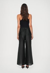 Black, wide-leg pants with a flowy, lightweight fabric, featuring an elastic waistband and a smooth texture, paired with heeled sandals.