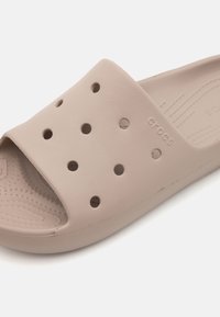 Beige slip-on sandal lavet af blød plast med ventilationshuller, struktureret fodseng og prægede logo på siden.