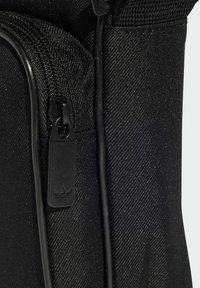 Borsa nera in tessuto con materiale testurizzato, chiusura con zip e logo impresso sul tirazip. Il design è minimalista e funzionale.
