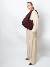 Vinjött vävd handväska med rundad form och bred rem. Modellen bär en creamfärgad oversize-tröja och beiga plisserade byxor.