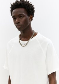 Hvid, kortærmet T-shirt med en afslappet pasform og rund halsudskæring. Har tekstureret stof og lagdelte sølvkæder.